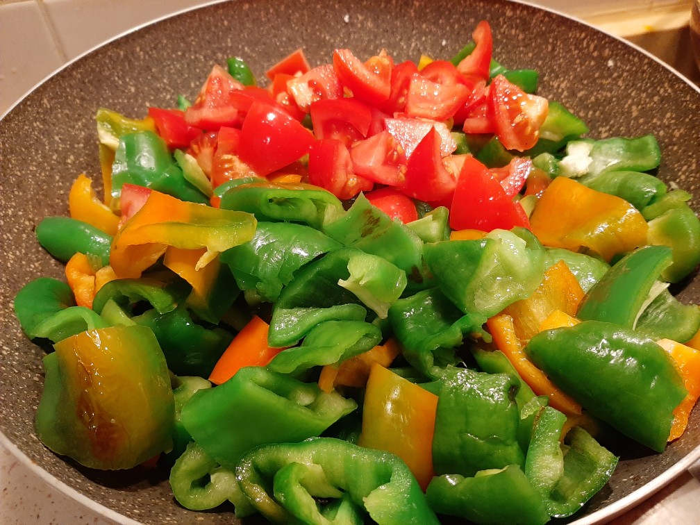 Лук и болгарский перец, тушущиеся на сковороде с небольшим количеством масла.