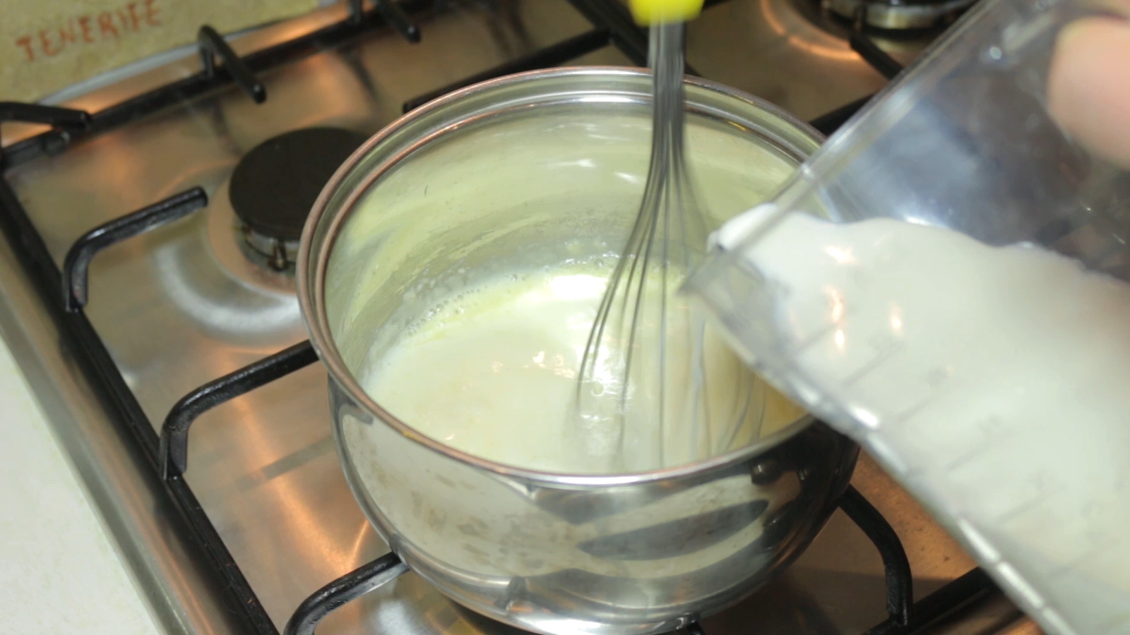 Белый бешамель соус варится в кастрюле, активно помешивая венчиком, густеет