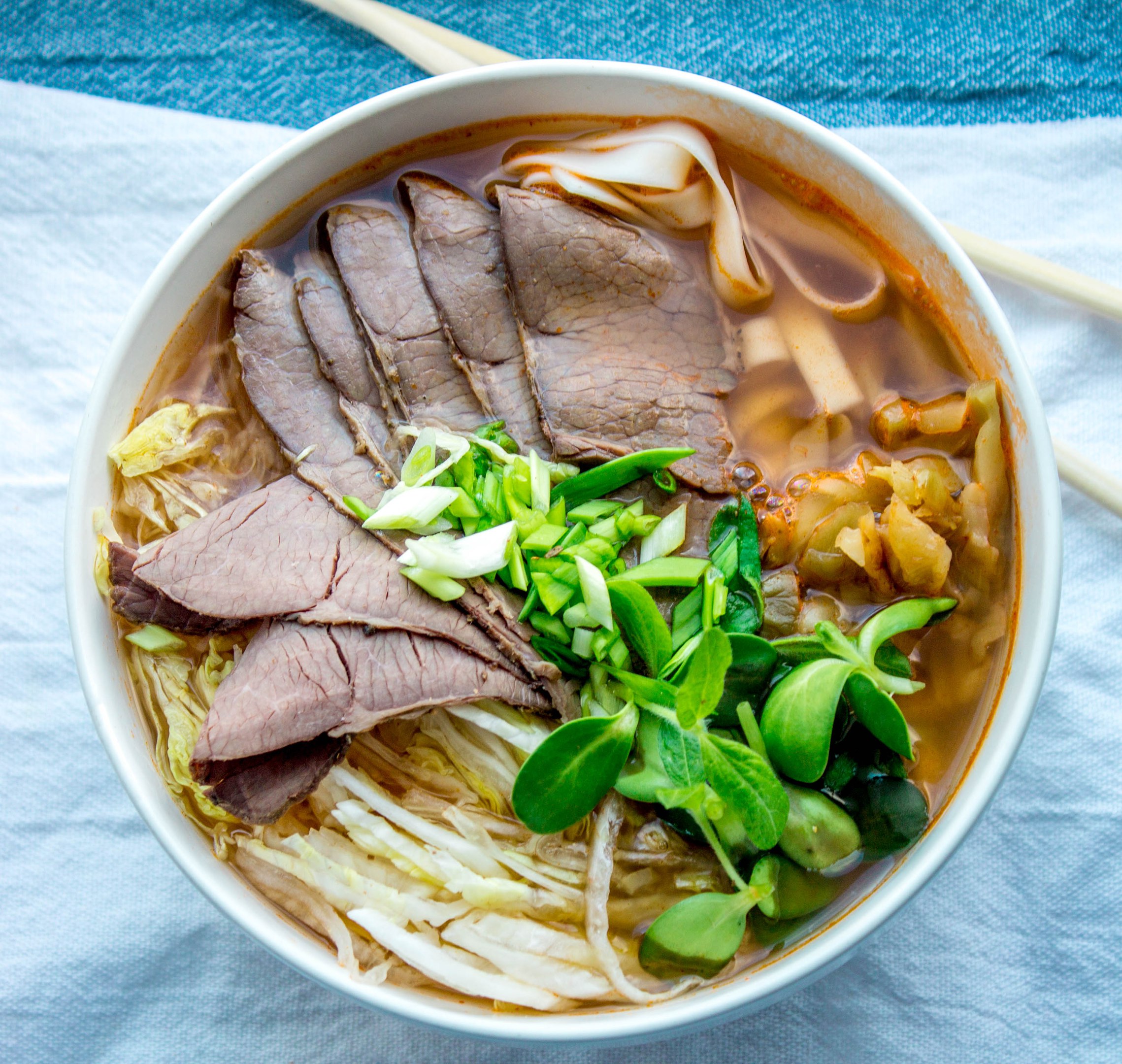 Заливание горячего бульона в миску с лапшой, говядиной и зеленью